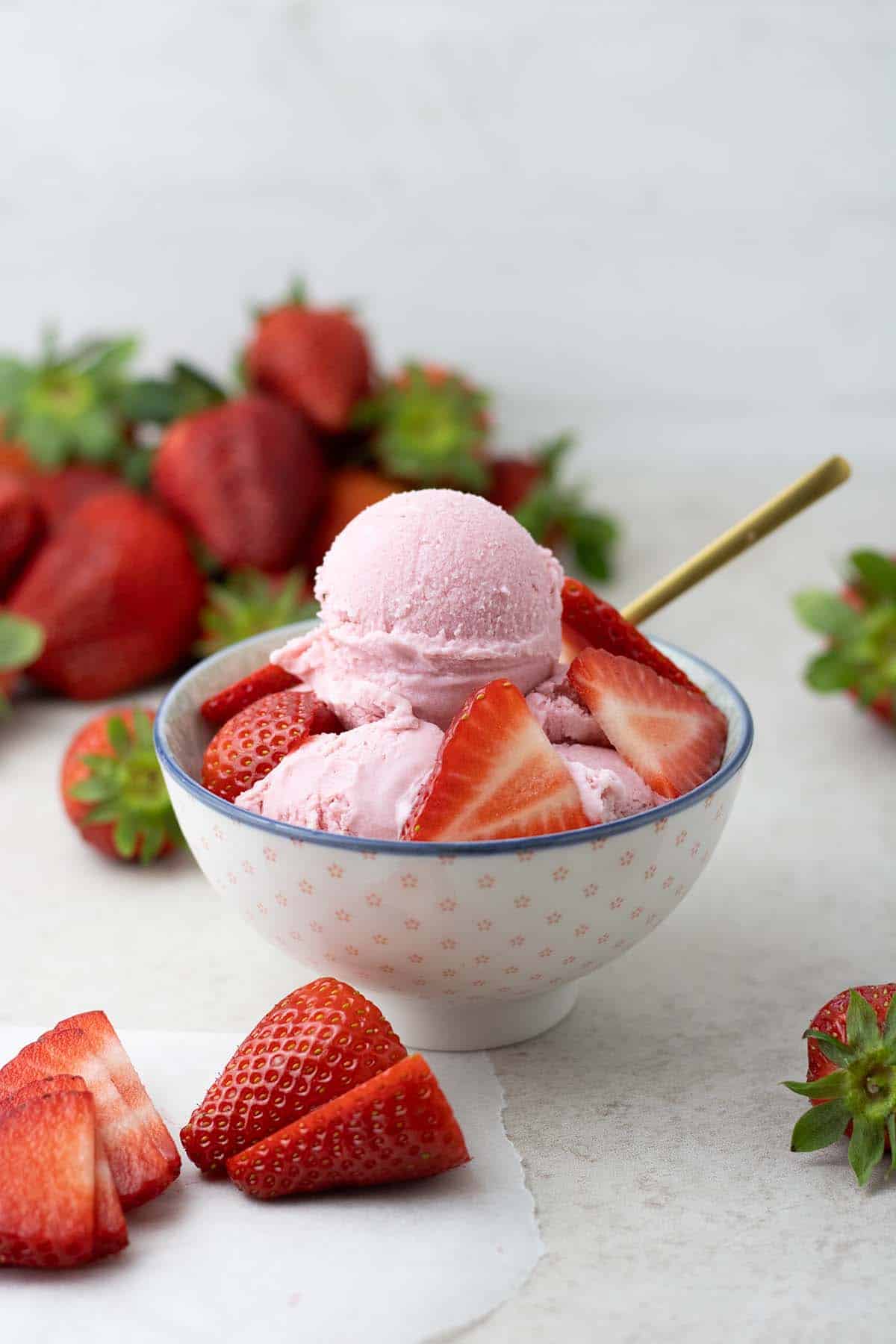 Strawberry ice cream in a bowl with strawberries laying around.