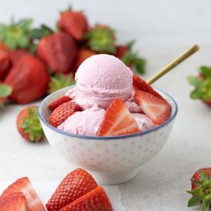 Strawberry ice cream in a bowl with strawberries laying around