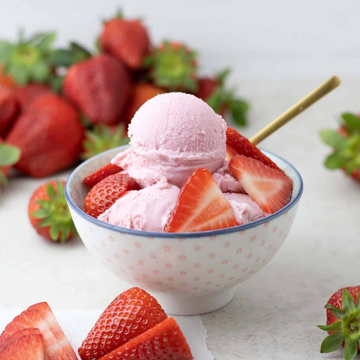 Strawberry ice cream in a bowl with strawberries laying around